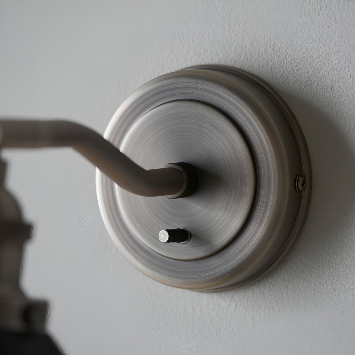 Close-up of the Endon Bramdale wall light's silver circular backplate with knurled toggle switch and adjustable arm mounted on a white wall.