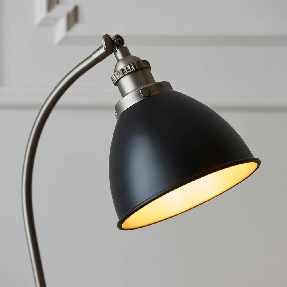 Close-up of Endon Bramdale table lamp head, matt black rolled-edge metal shade with aged pewter adjustable knuckle and curved arm against a light grey wall.