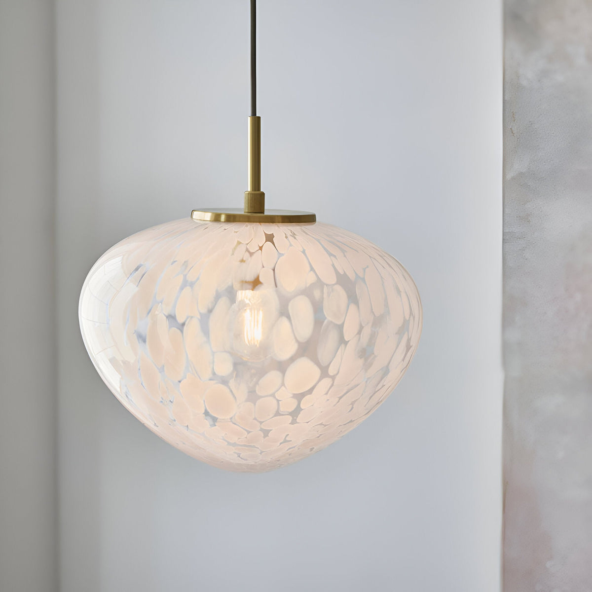 Calloway Pendant in brass and white, a single-light dome fixture with speckled confetti glass shade and satin brass fittings, shown lit.