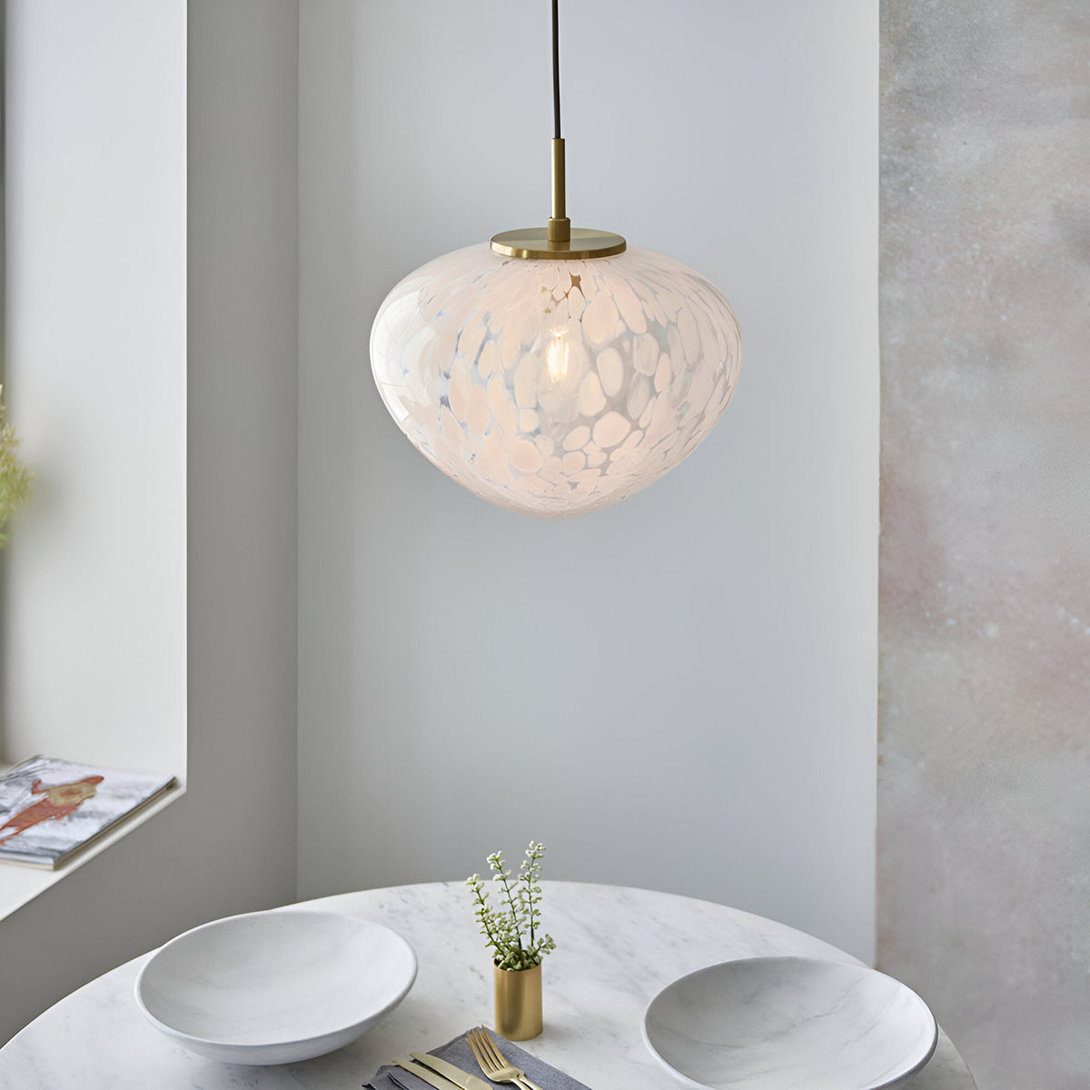 Calloway Pendant in brass and white, single-light fixture with speckled confetti glass shade, hung above a marble dining table.