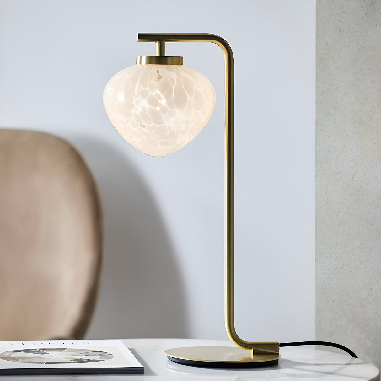 Endon Calloway table lamp in satin brass with a slim upright arm and white confetti blown glass shade, styled on a marble surface beside a chair.