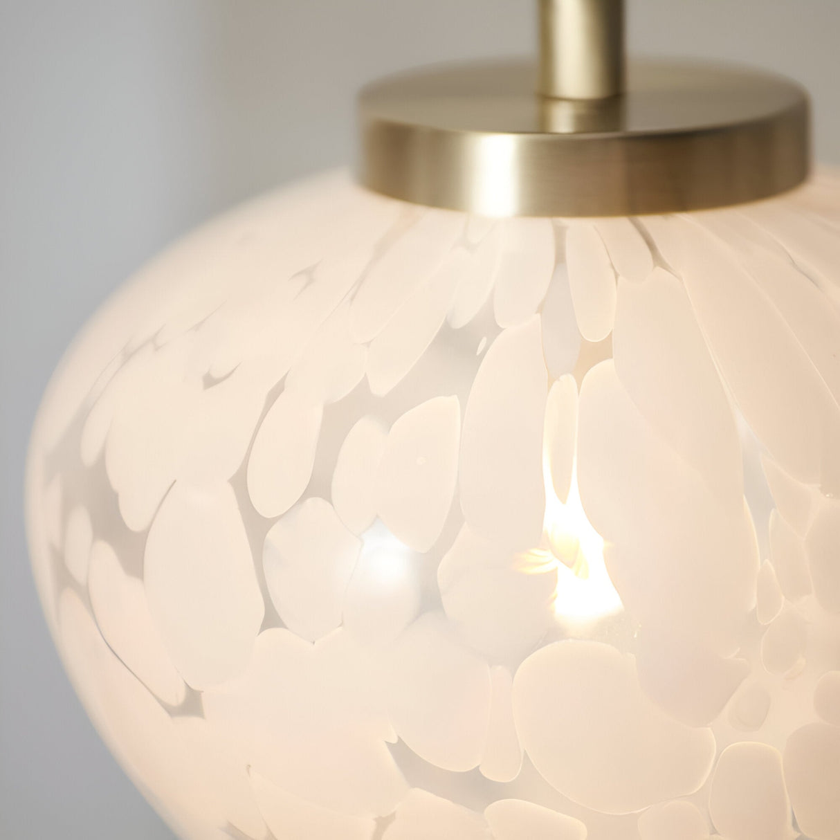 Close-up of the Endon Calloway table lamp showing its white confetti blown glass shade and satin brass fitting with a lit G9 bulb inside.