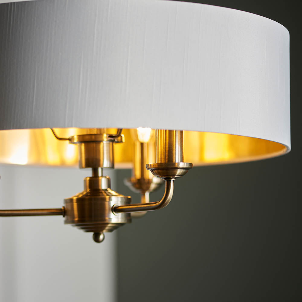 Close-up of Endon Brenley 3 Light Pendant showing antique brass fittings, white fabric shade with gold metallic lining catching a warm glow.