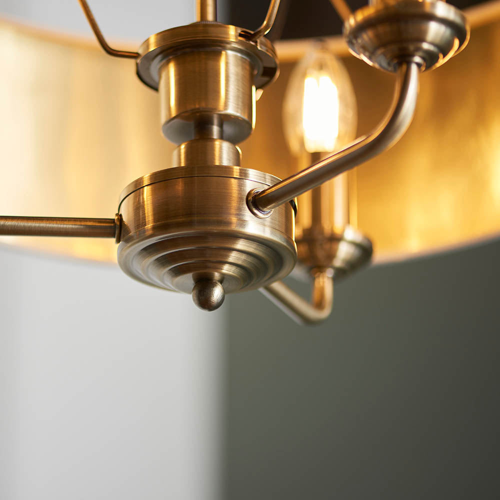 Close-up of the Endon Brenley 3 Light Pendant showing antique brass fittings, tiered central boss and curved arms with a gold-lined shade interior.