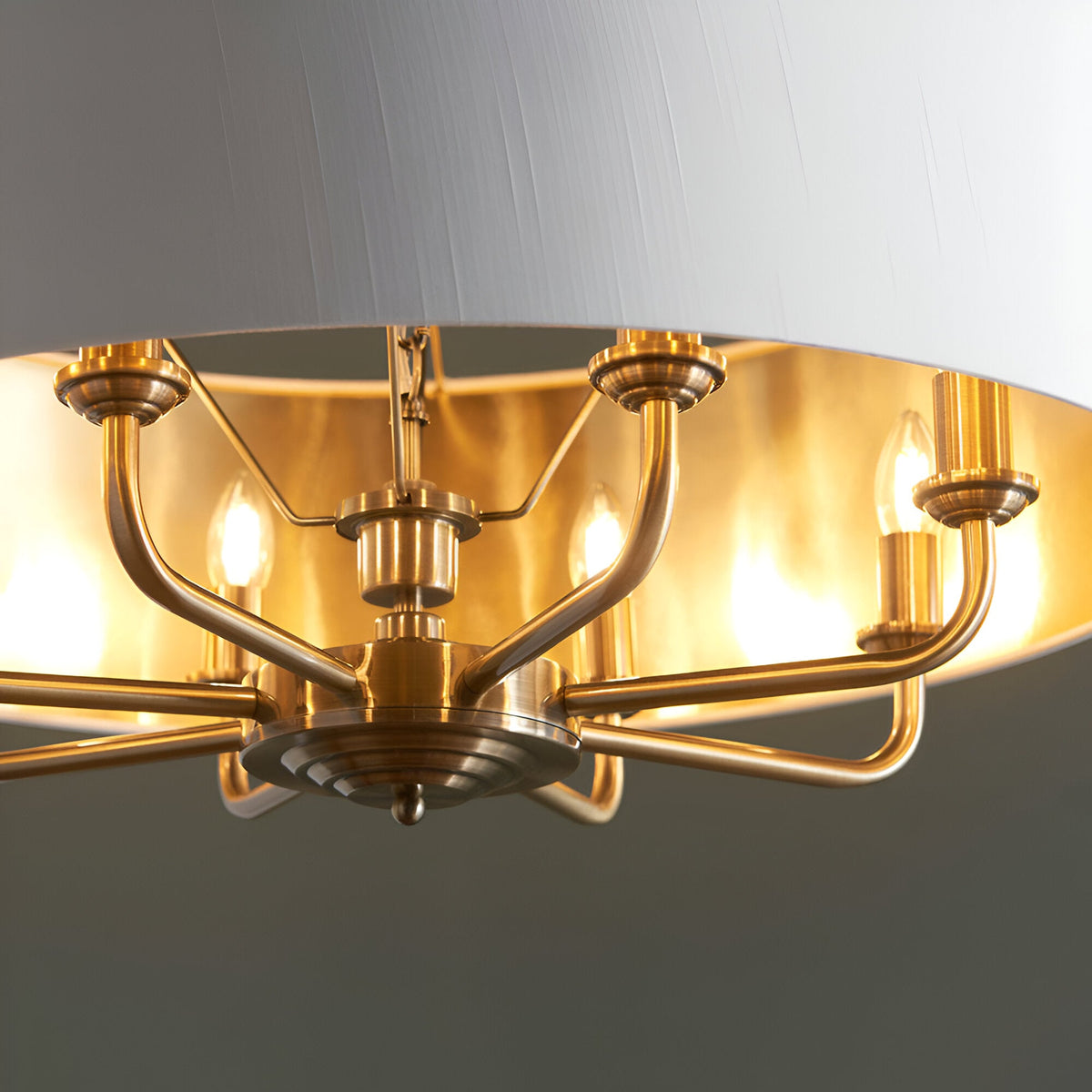 Close-up of Endon Brenley 8 light pendant showing antique brass arms, candle lamps and gold-lined vintage white fabric shade interior.