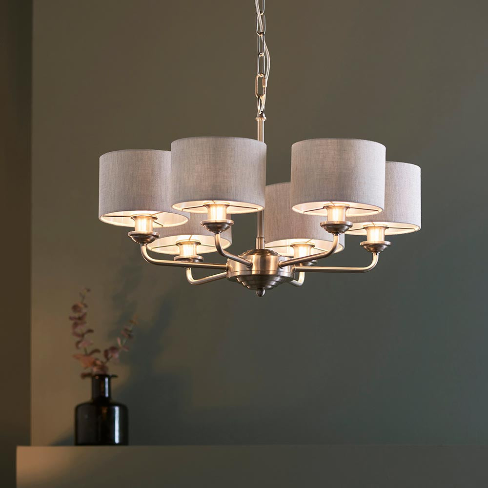 Brenley six-light pendant with brushed chrome arms and grey fabric drum shades, hung on a chain in a room with muted green walls.