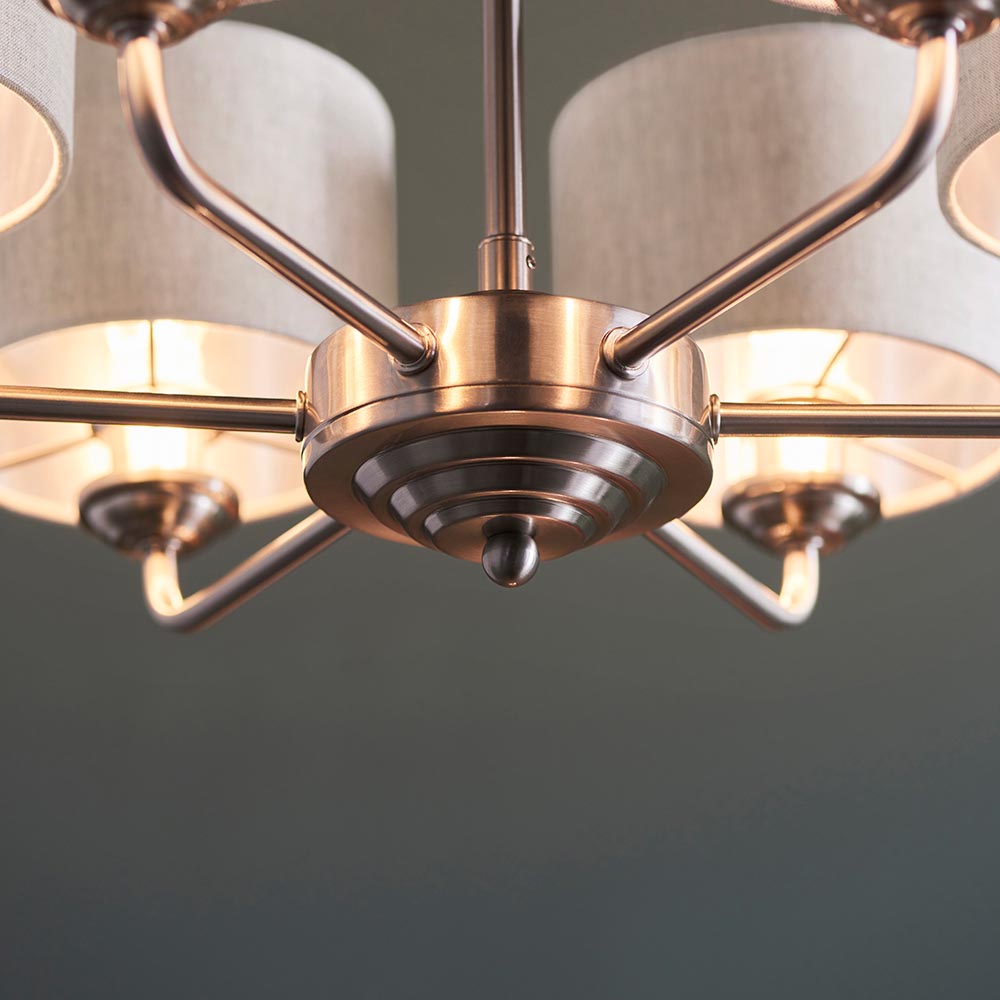 Close-up of the Brenley 6 light pendant's brushed chrome centre hub with tiered detailing and six angled arms holding natural linen shades.