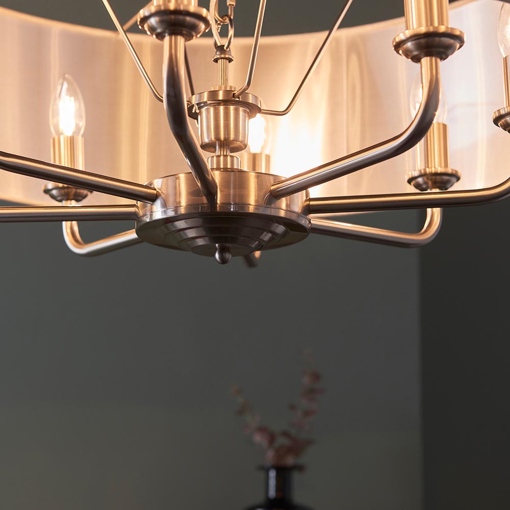 Close-up of the Endon Brenley 8 light pendant showing its chrome and brass central hub, curved arms and metallic-lined fabric shade above a dark room.