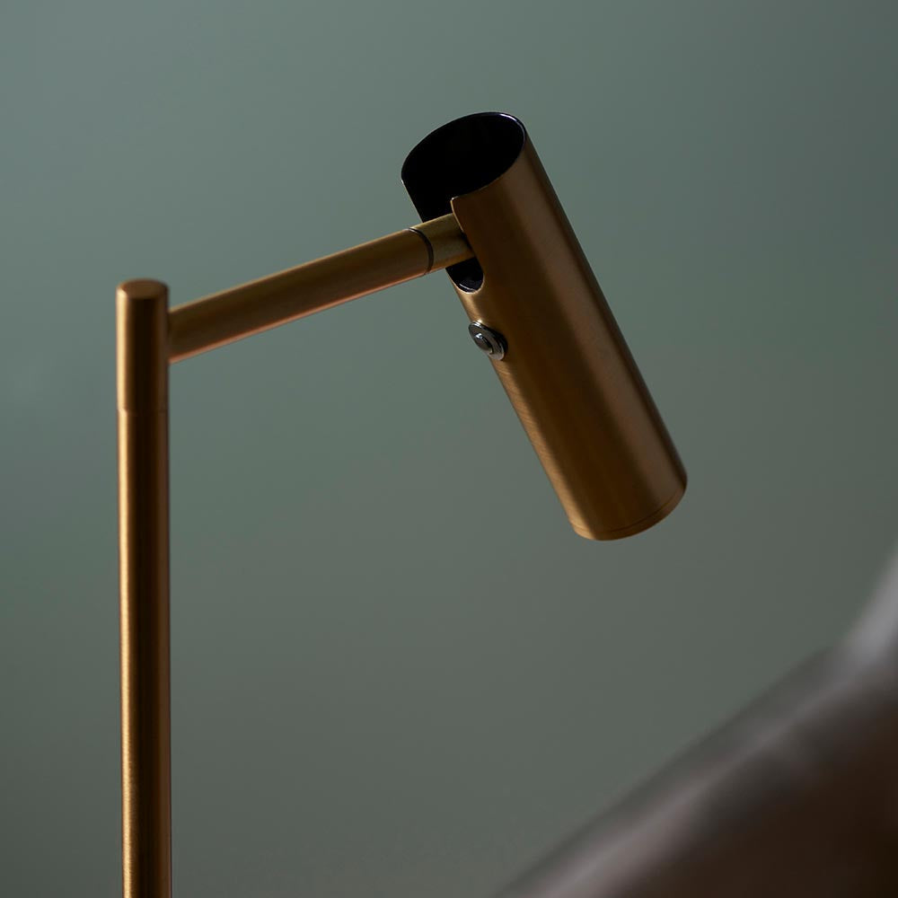 Close-up of the Endon Brackbourne floor lamp's adjustable brass cylindrical head and arm, with push button dimmer switch, against a soft green backdrop.