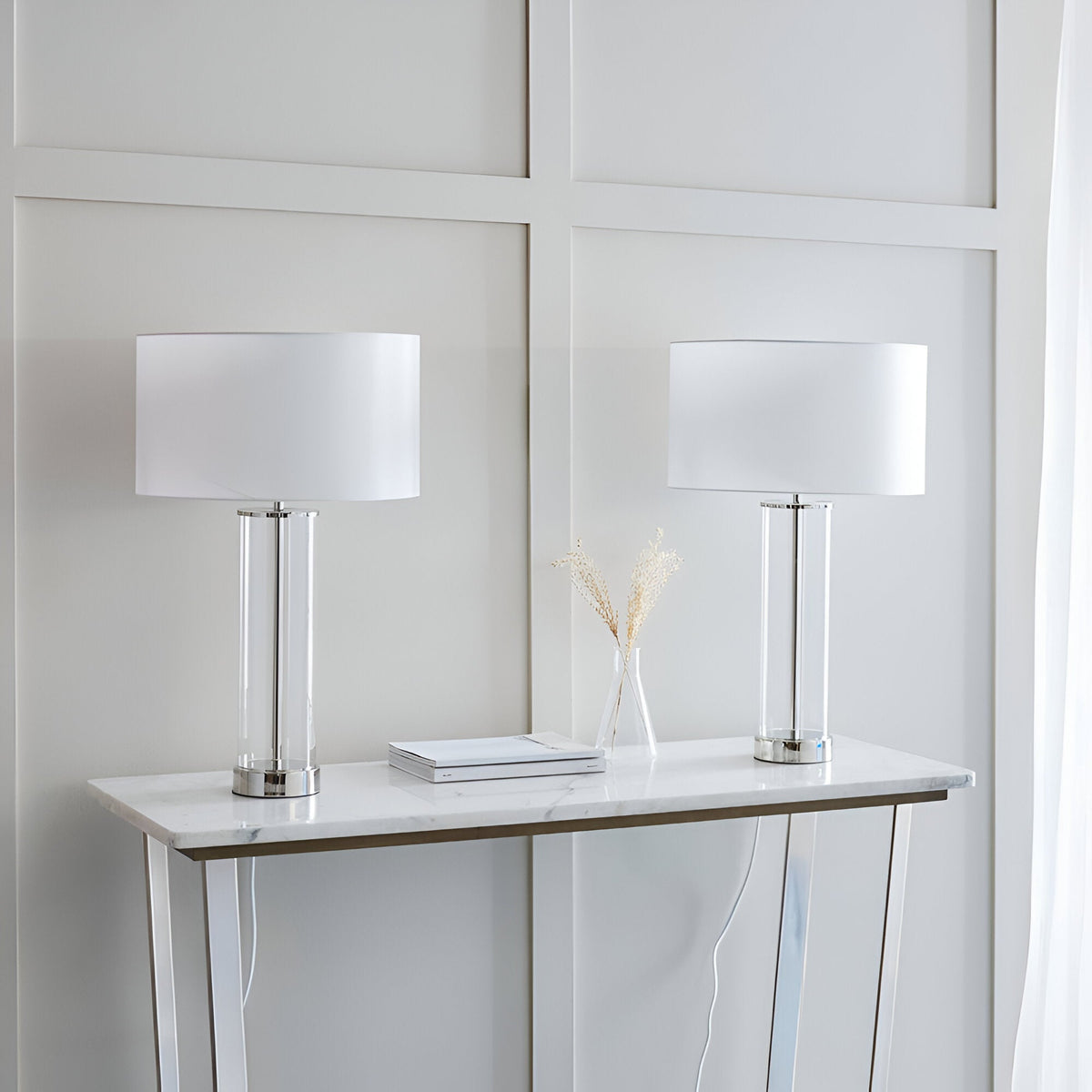 Endon Caldley twin pack table lamps with clear cylindrical glass bases, nickel fittings and white drum shades, styled on a marble console table.
