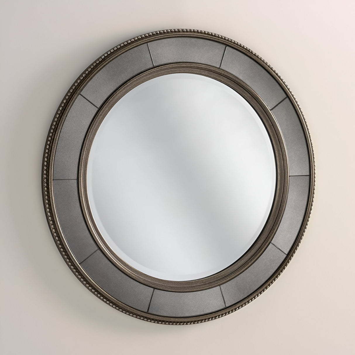 The Solix Circle Wall Mirror - 92cm - Antique Silver/Bronze, featuring a decorative dark gray frame with antique silver and bronze accents, hangs gracefully on a beige wall. Its pattern of alternating smooth and textured sections infuses vintage charm, adding an elegant touch to the mirror's design.