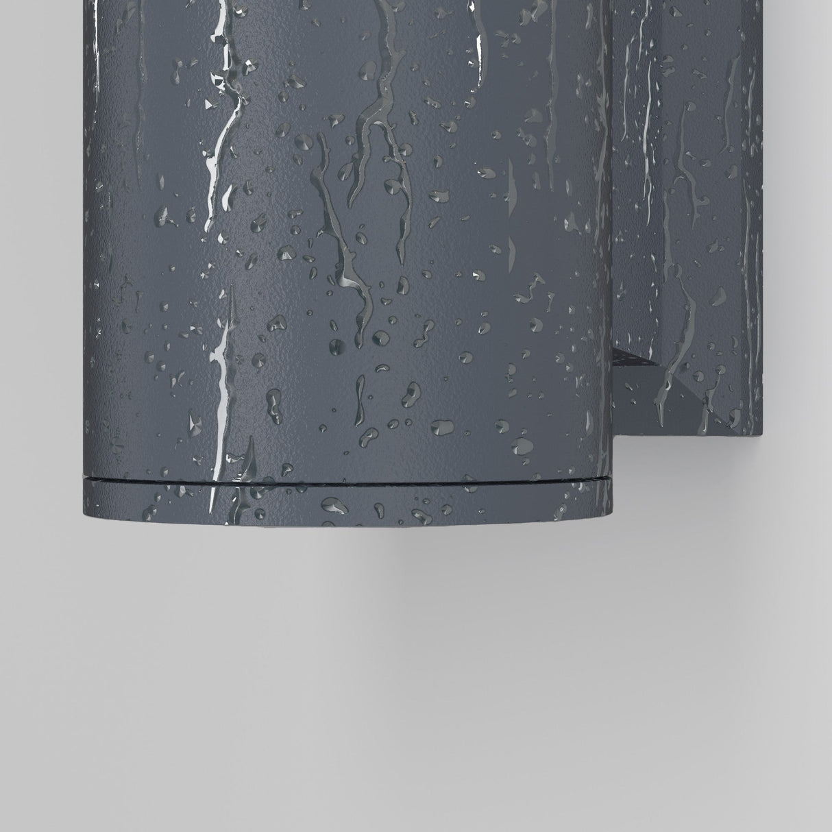 The Bowery Outdoor 1 Light Wall Light - Grey (O574WL-01GR) is a dark gray cylindrical fixture with a raindrop-textured surface, offering durability and elegance when mounted on a light gray wall.