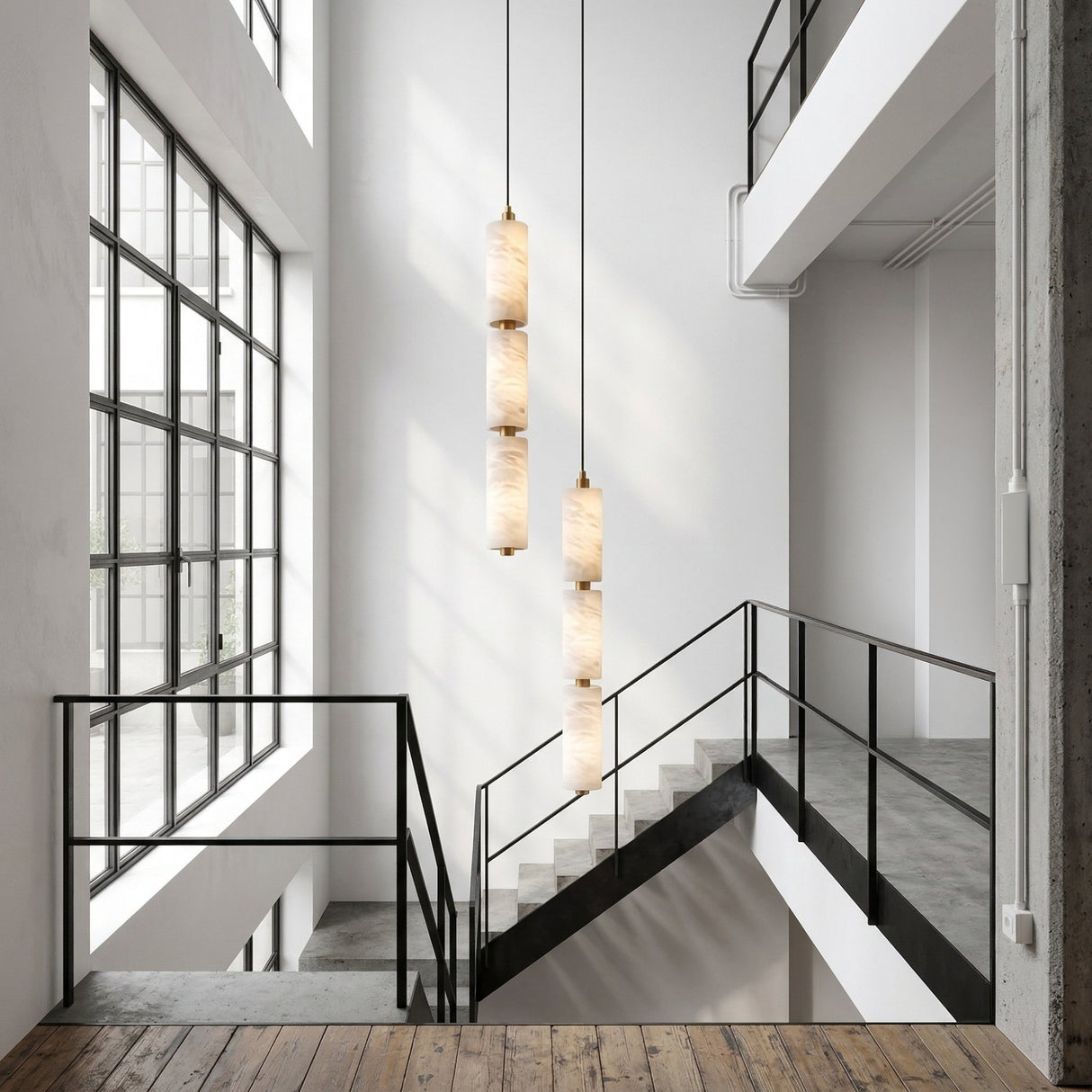 A modern, minimalist interior with large industrial-style windows, a concrete staircase with black railings, a wooden floor in the foreground, and three Ardent LED Large Column Alabaster Single Pendant Lights in soft white & brushed brass.