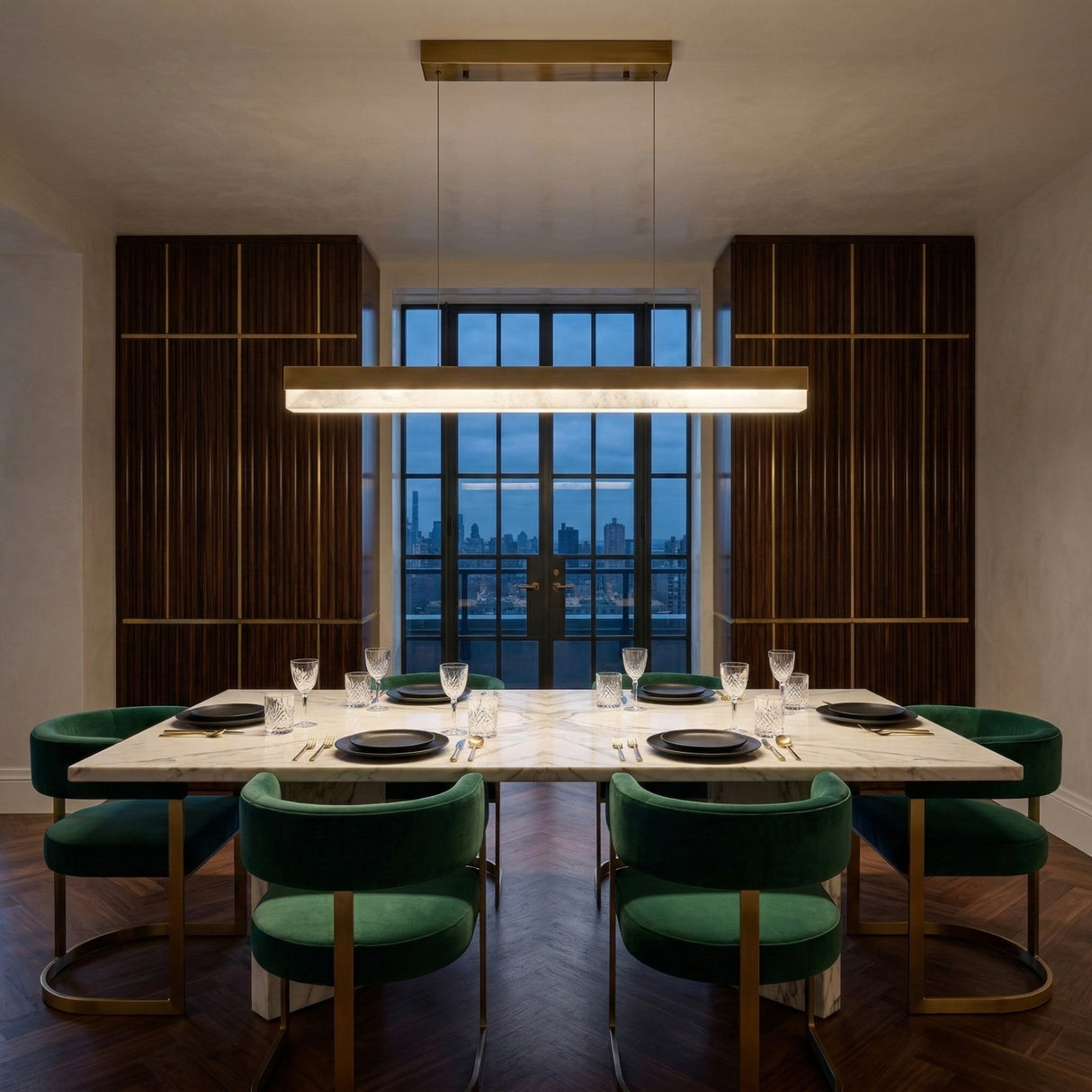 Niori Linea LED Alabaster Linear Chandelier in brushed brass above a marble dining table with green velvet chairs in a wood-panelled room.