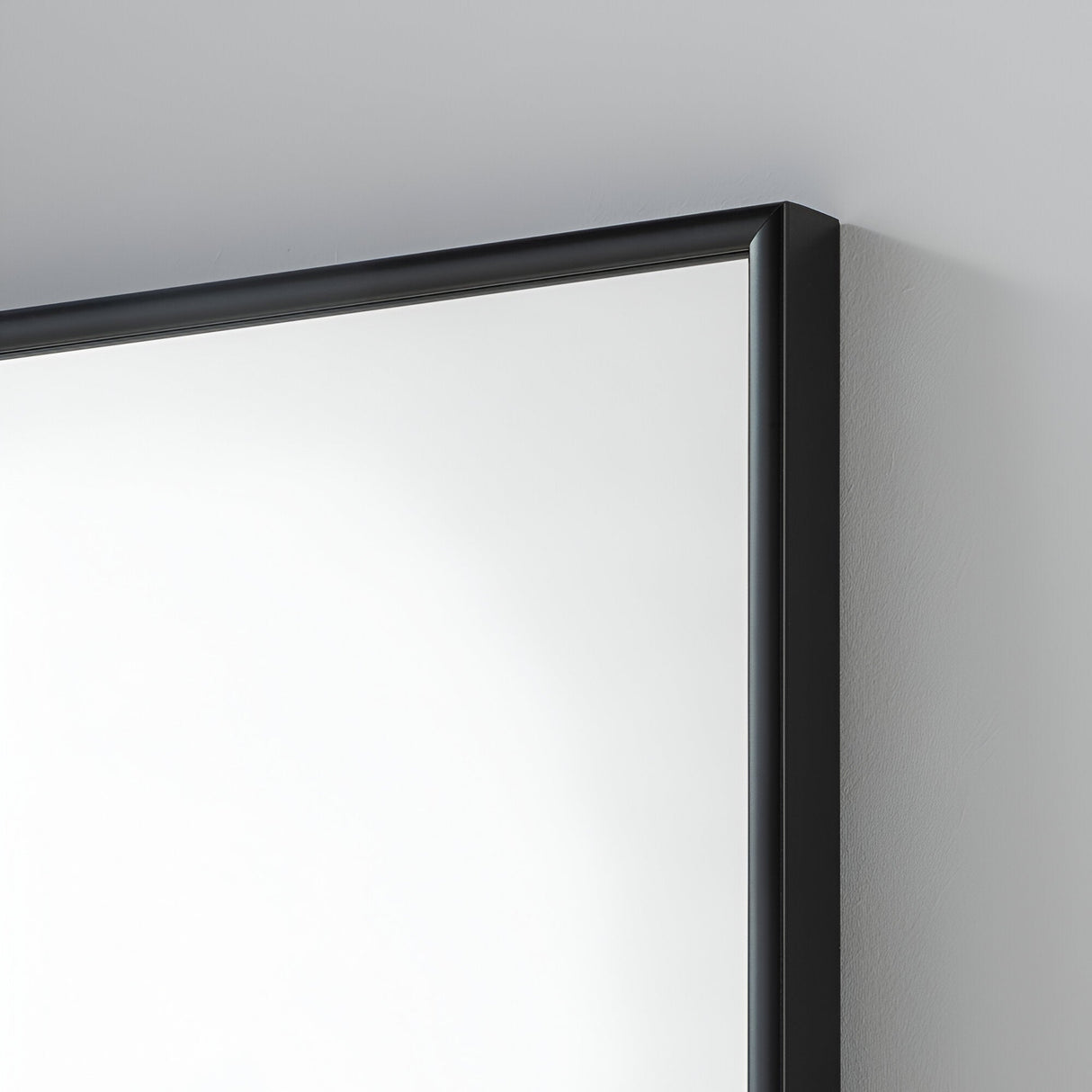 Close-up of the Mirra Rectangle Wall Mirror - Black, featuring a sleek black frame, mounted on a light gray wall. Its reflective surface brightens the space, adding to its minimalist charm—a perfect element for contemporary home decor.