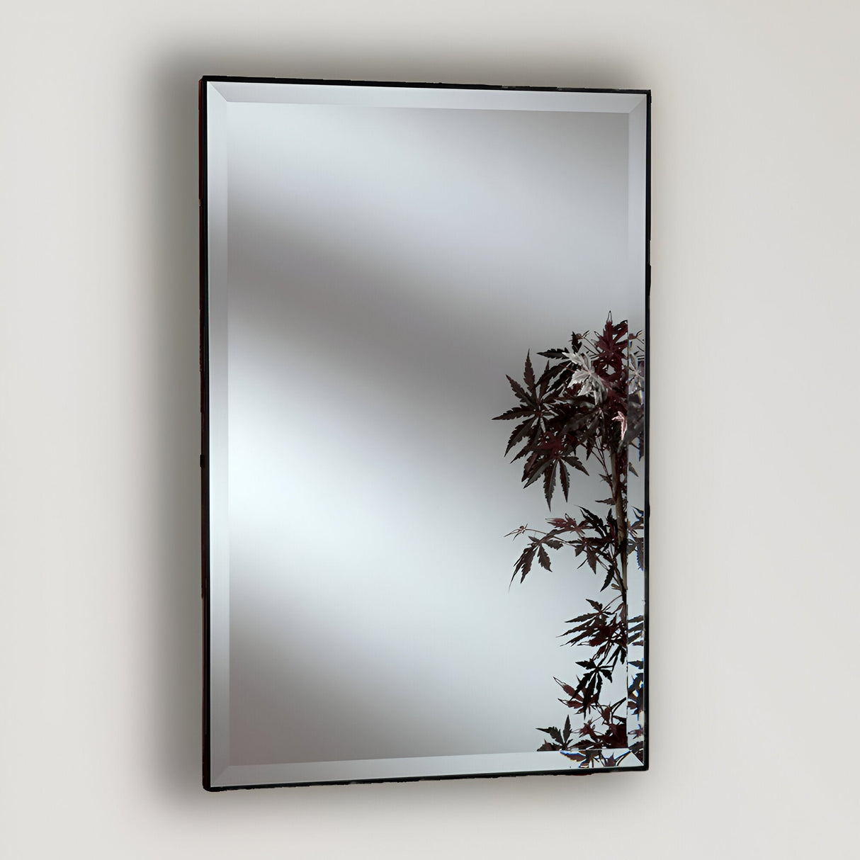 The Empyra Rectangle Wall Mirror - Black, featuring a beveled edge and a black wooden frame, reflects light. An artistic botanical motif of leaves adorns the bottom right corner, adding an elegant touch to any plain wall.