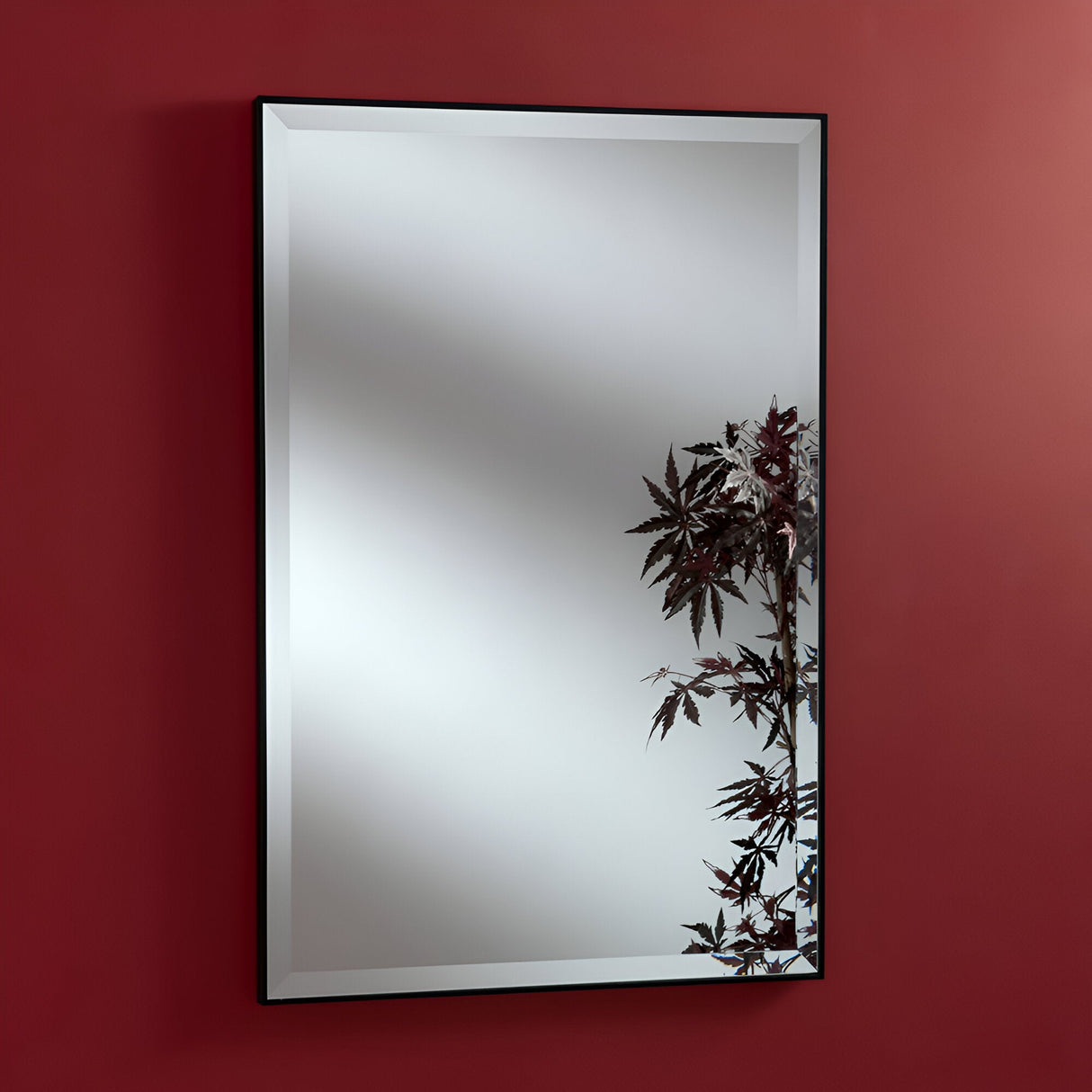 An Empyra Rectangle Wall Mirror - Black hangs on a red wall, featuring a botanical motif in the bottom right corner. The reflection is blank except for this decorative design.