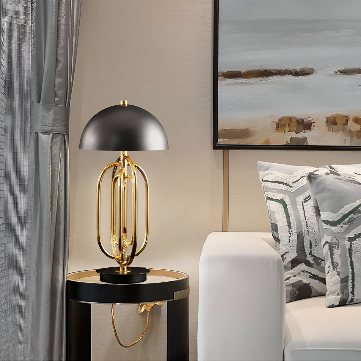 The Ascot 4 Light Large Table Lamp in black & gold sits on a round side table beside a white sofa with patterned pillows, adding modern Art Deco style to a neutral-toned living room with abstract wall art.