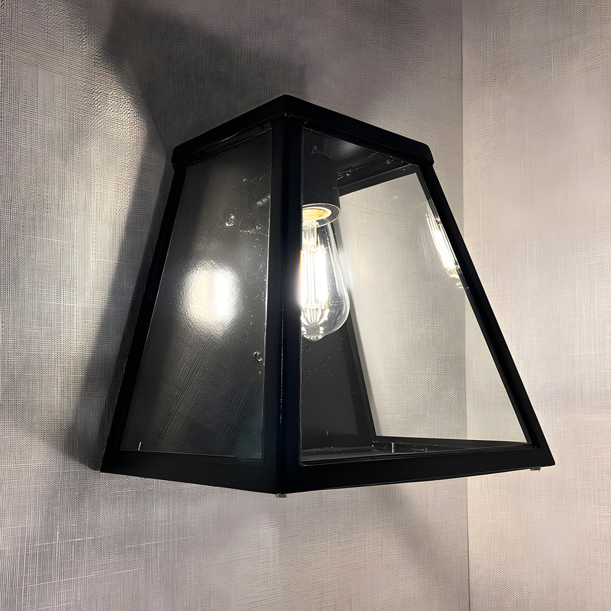Contemporary Galvanised Steel Bulkhead Wall Light in black, tapered glass panels with visible bulb, mounted against a light grey textured wall.