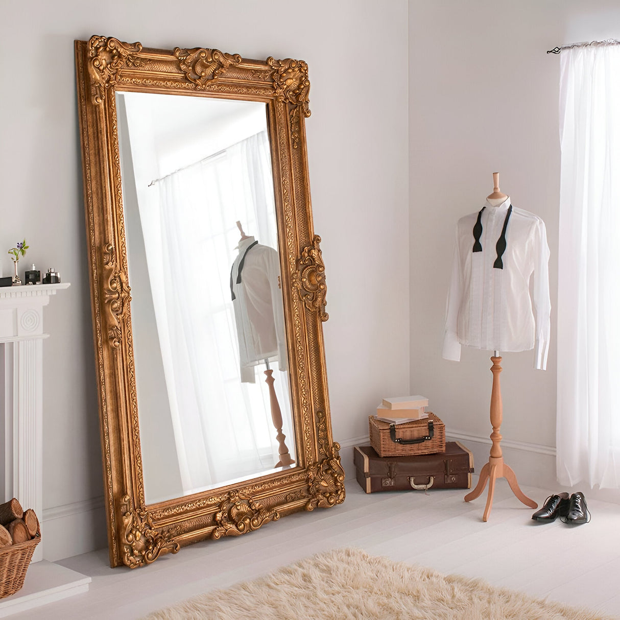 A Crystalix Leaner Mirror in dark gold, measuring 201x100cm, rests against a white wall in a bright room. Nearby, a mannequin is dressed in a white dress shirt and black bow tie. A pair of shoes and suitcases are positioned on the floor, which is covered by a soft rug.