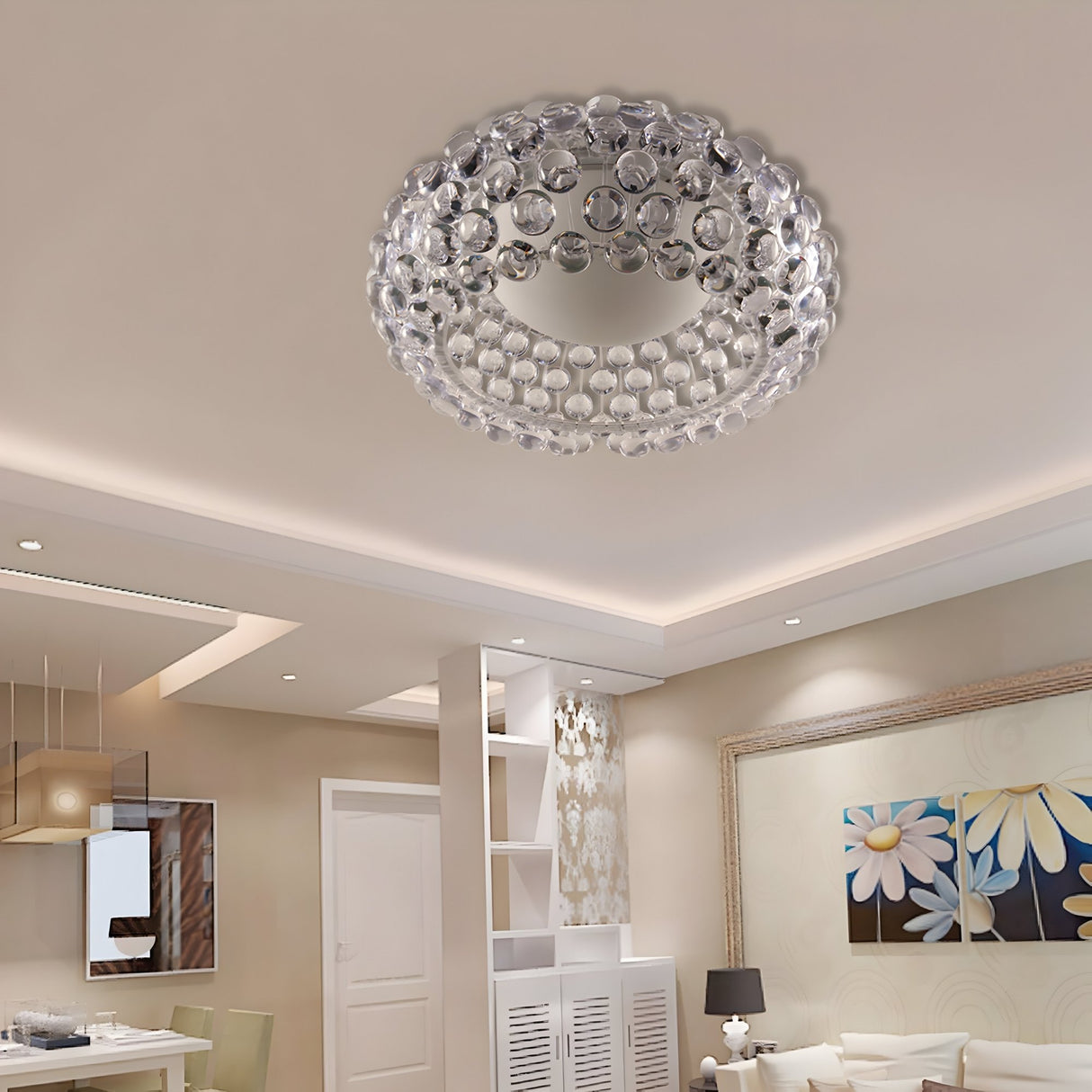 A modern living room features a Briller LED Ceiling Light - Transparent, round crystal chandelier, recessed lighting, dining area, large floral painting, and elegant neutral-toned decor for a chic contemporary look with a gem-like glow.