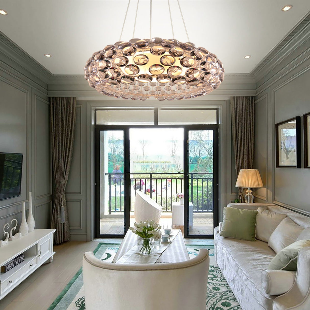 Elegant living room with gray walls, cream sofa, and white coffee table topped with flowers. Modern elegance shines from the Briller LED Large Suspension Light - Clear above, while sliding doors open to a balcony garden view.