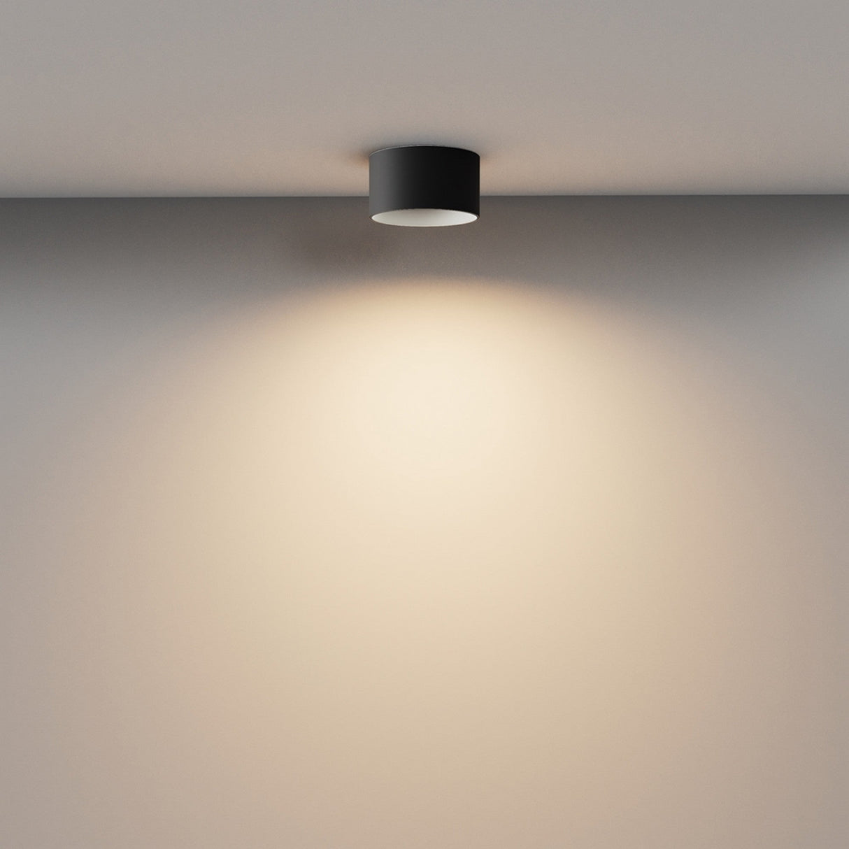 The Vega LED Round Surface Downlight 12W 3000K in black casts a warm, subtle glow on a light wall, forming a gentle gradient of light and shadow—ideal for modern interiors.