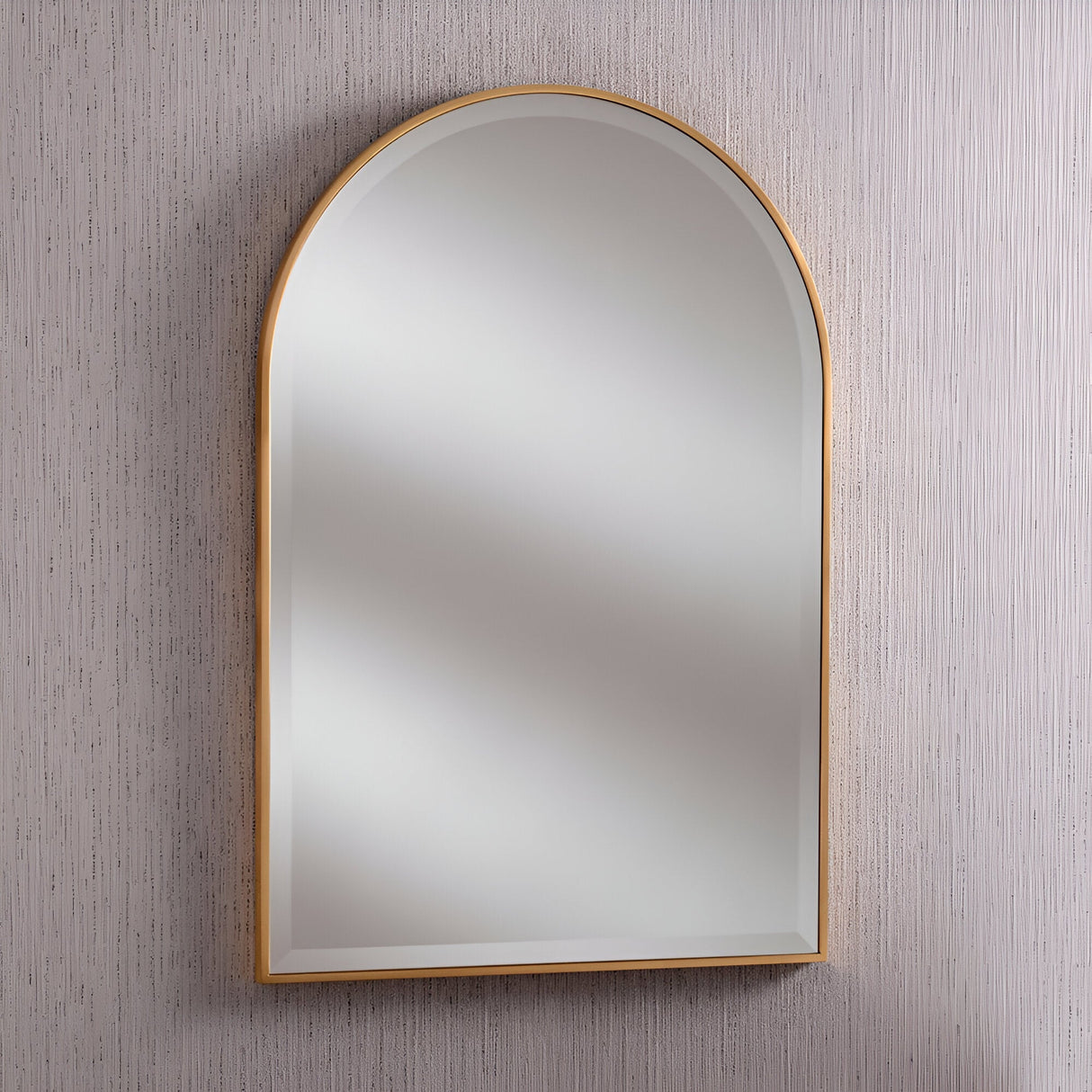 The Camden Arched Wall Mirror Gold - 93x63cm exudes timeless luxury as it reflects light, elegantly set against a textured, light gray wall.