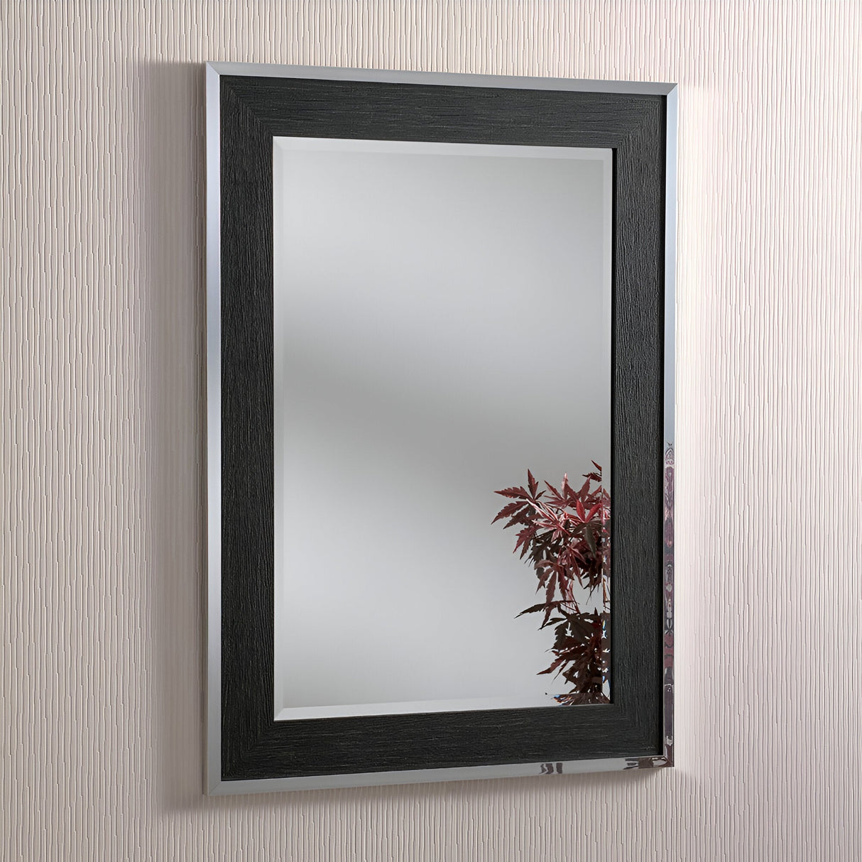 The Zennia Rectangle Wall Mirror - Black/Silver reflects part of a plant with red leaves, perfectly complementing the textured, light-colored wall in the background and blending seamlessly into contemporary decor.