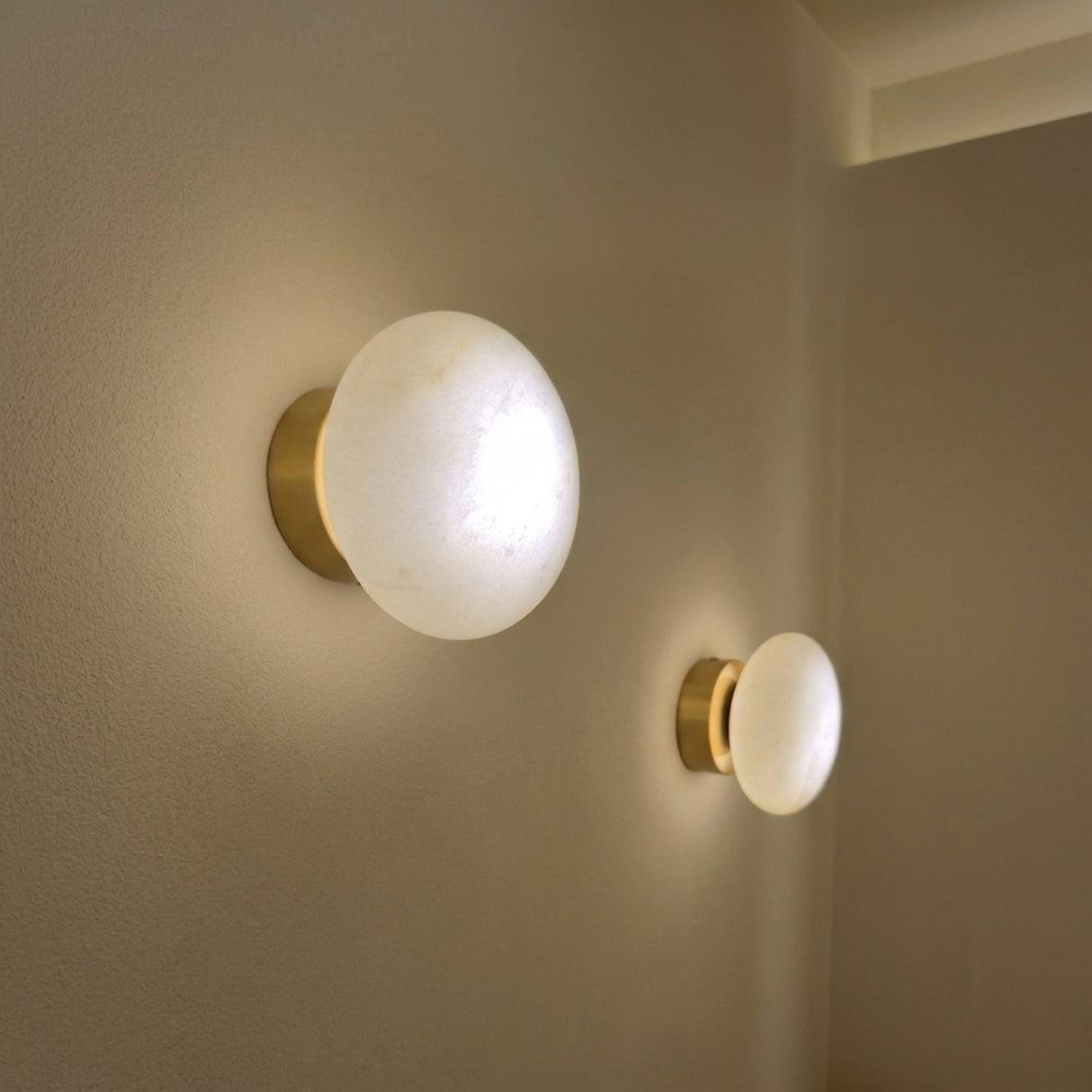 Solenne LED Halo Alabaster Wall Light in Brushed Brass, domed stone discs glowing warmly on a brass backplate, shown as a pair mounted on a wall near a doorway.