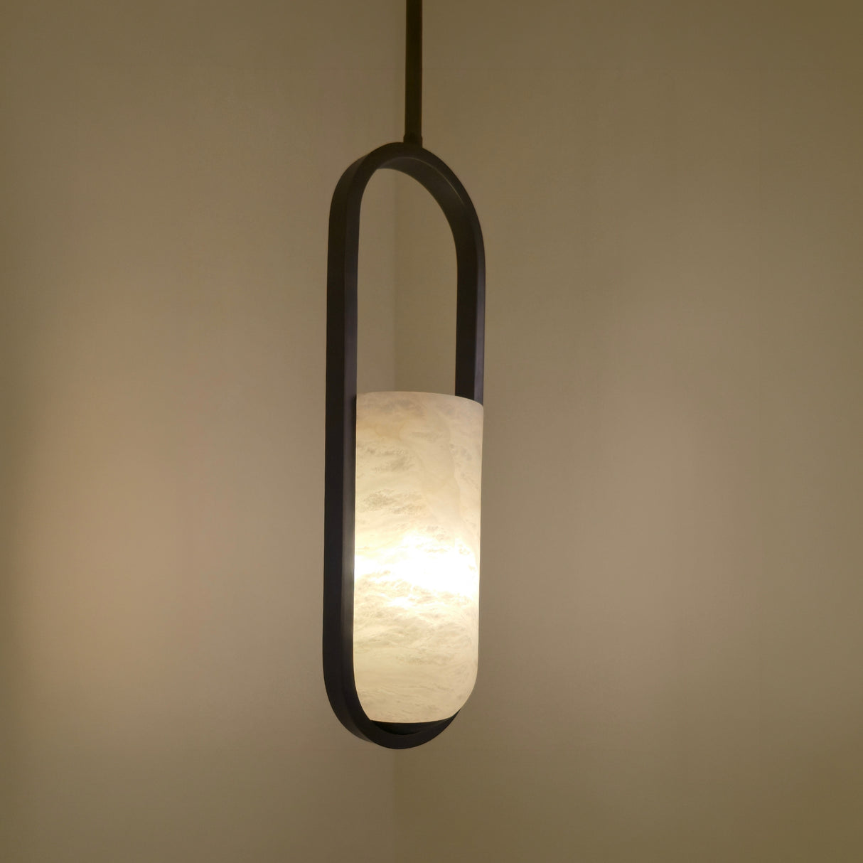 Eliona Capsule Alabaster Pendant Light in matt black, a single cylindrical alabaster shade lit warmly within an oval capsule frame, shown against a neutral wall.