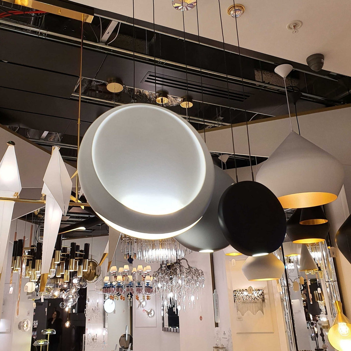 The showroom displays modern hanging lights, including the Cosmos 3 Light LED Bar Pendant - V2, all showcased beneath mirrored and reflective ceiling features.