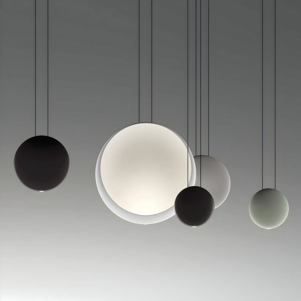 Five Cosmos LED Large Pendant Lights of different sizes and shades hang from the ceiling against a neutral background, creating a modern minimalist lighting arrangement with soft ambient light.