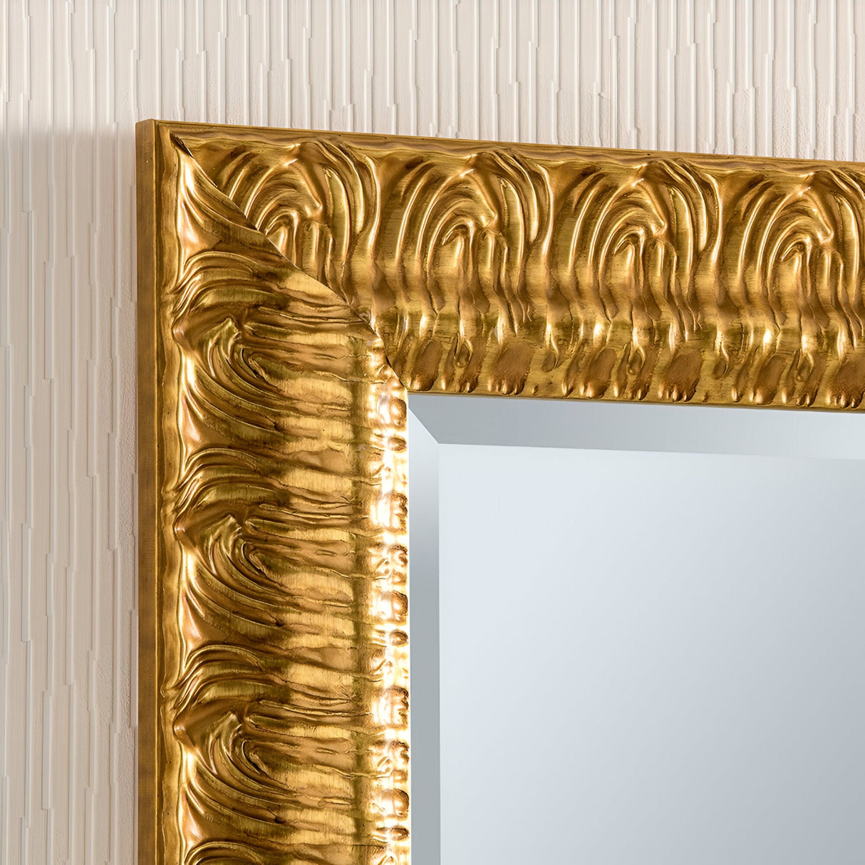 Close-up of the Crown Rectangle Wall Mirror in dark gold, showcasing its ornate frame with intricate, wavy patterns. The backdrop reveals a textured beige wall.