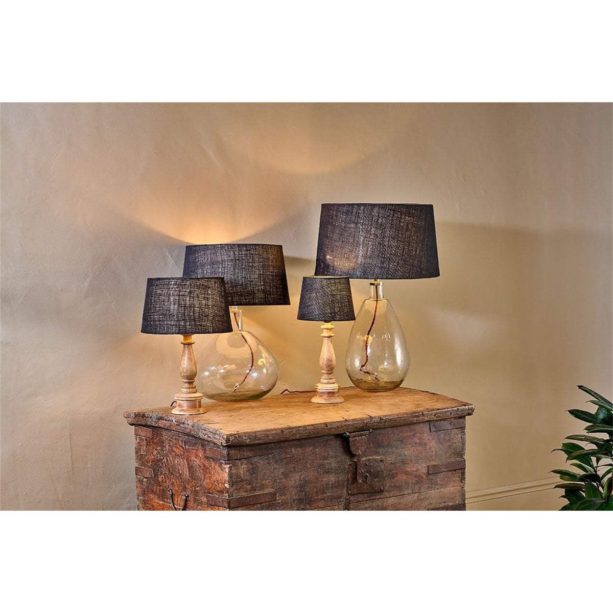Dia Large Jute Lampshade in ink shown as tapered drum shades on wooden table lamps with turned bases and glass bases, set on a wooden chest in a living room.