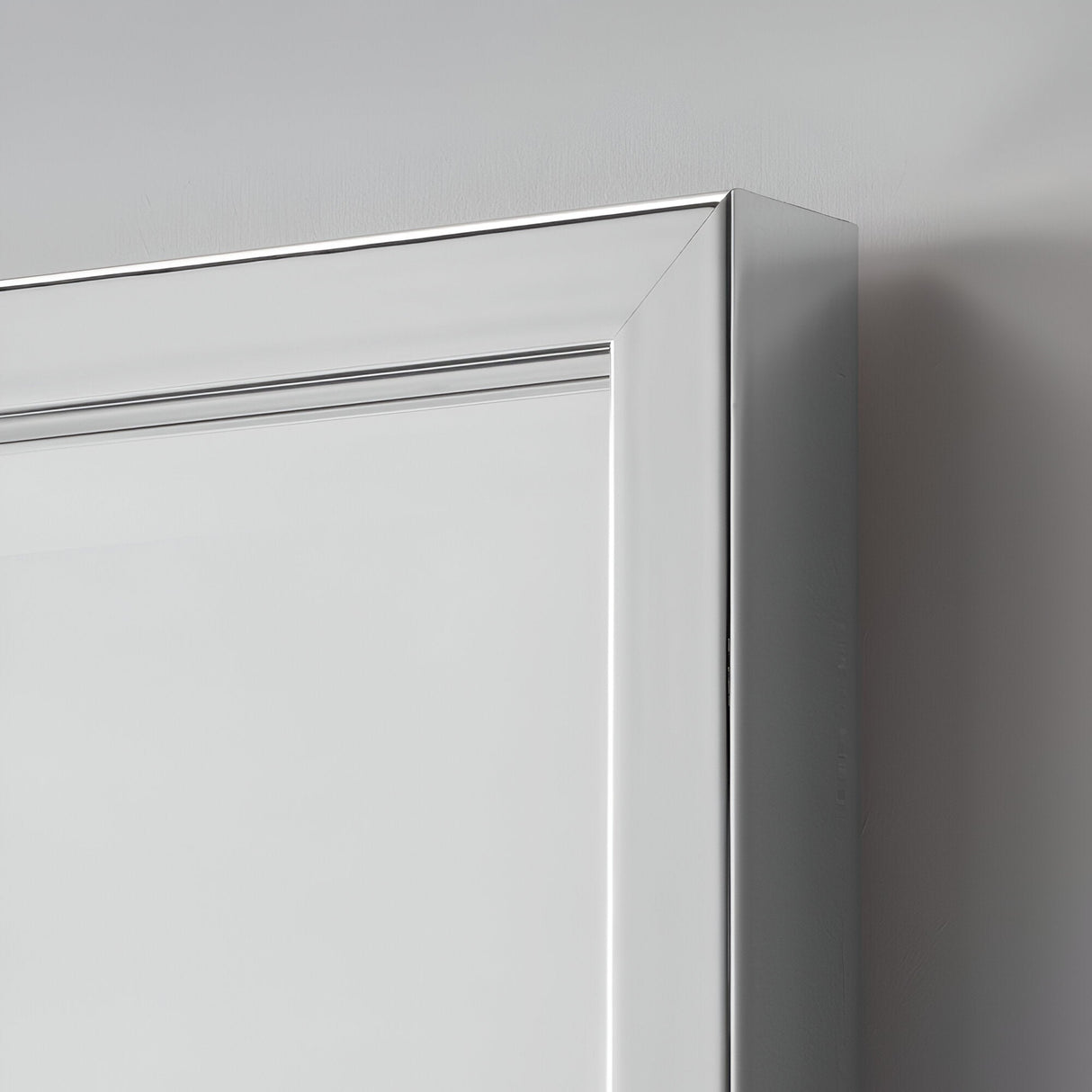 Close-up of the corner of a silver frame with a minimalist design against a light gray background. The smooth, sleek lines and metallic finish give it a contemporary look, echoing the industrial-style elegance of the Dalston Rectangle Wall Mirror.