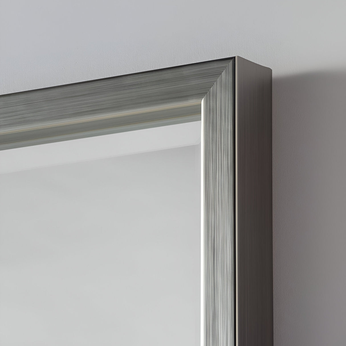 Close-up of a sleek, metallic picture frame corner against a plain background. The Dalston Rectangle Wall Mirror - Grey features a shiny, brushed metal finish and elegant design, embodying modern sophistication with its streamlined appearance.