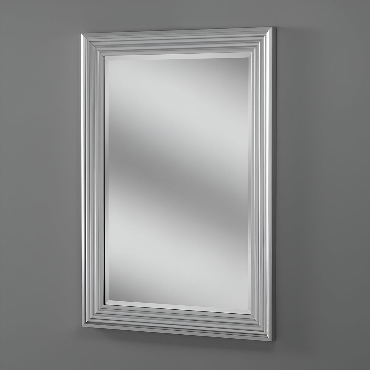 The Deco Rectangle Wall Mirror - Matt Silver graces the gray wall, its modern design accented by a silver frame with multiple beveled layers for added elegance. The empty reflection in the mirror emphasizes its sleek and polished appearance.