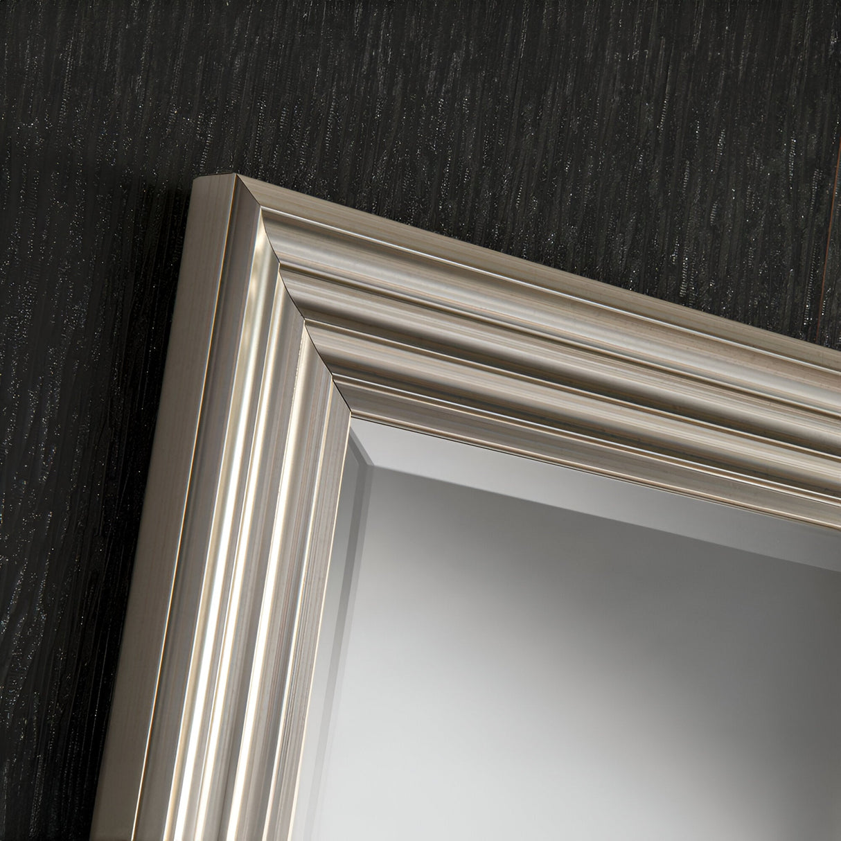 Close-up of the Deco Rectangle Wall Mirror in Silver, featuring a metallic, ridged frame against a textured dark wall. The polished silver finish enhances its modern simplicity, adding an elegant touch to the reflective surface.