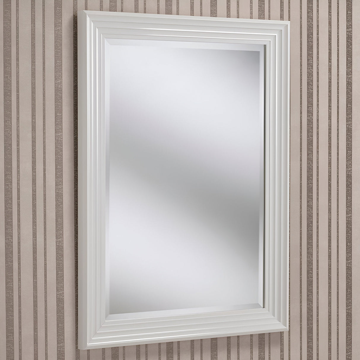 The Deco Rectangle Wall Mirror - White, known for its minimalist design, is mounted on a wall adorned with vertical beige and white stripes. Its white, layered frame enhances the reflective surface, which reveals a subtly blurred background.