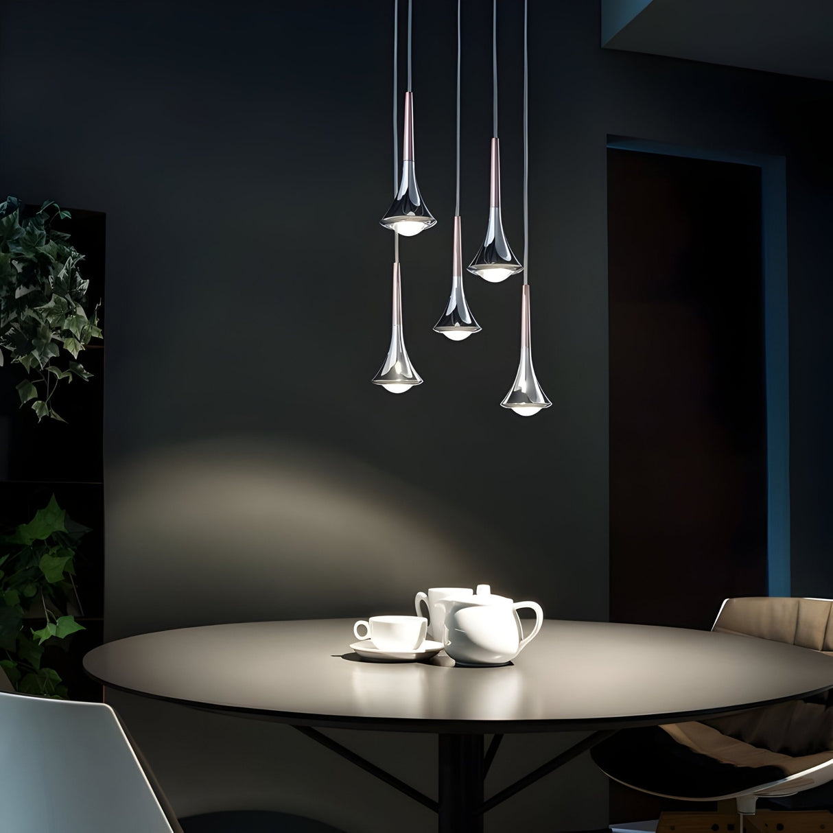 A modern dining area with a round table set for tea, featuring a teapot, cups, and saucers. Five Droplet LED Pendant Lights in white & black hang above the table. A plant adds to the minimalist, cozy vibe in the background.