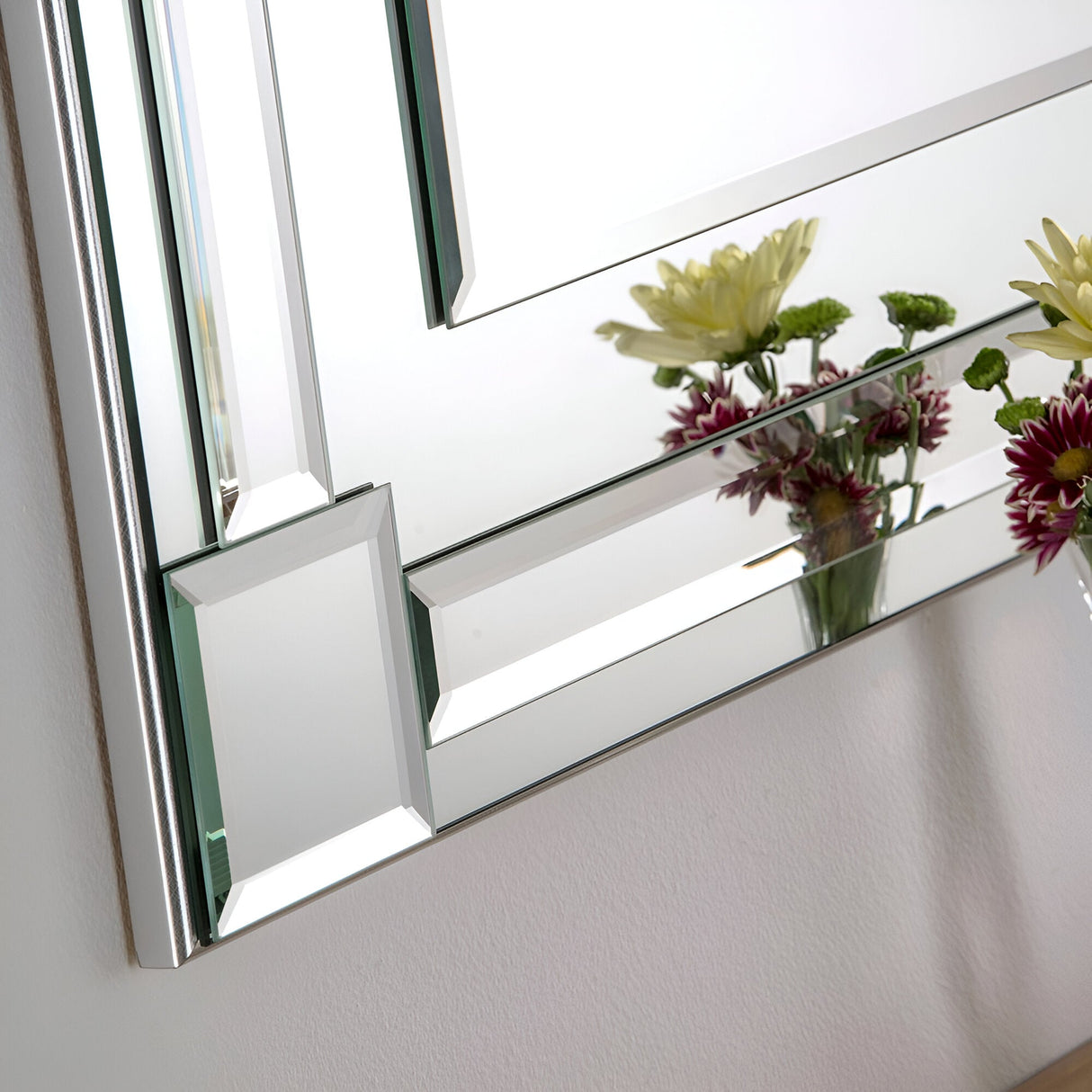 The Glowis Rectangle Wall Silver mirror, measuring 117x84cm, features a tasteful silver frame and beveled edges, perfectly reflecting a vase filled with vibrant yellow and purple flowers. This arrangement adds a lively splash of color to an otherwise plain wall, beautifully enhancing the minimalist decor.