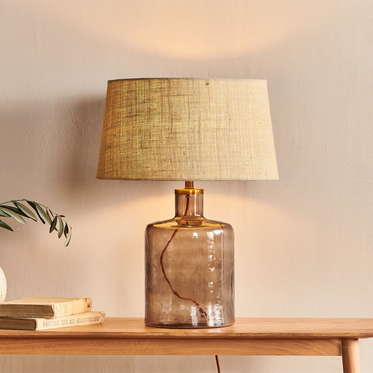 Edina Small Recycled Glass Table Lamp Base in smoke brown with hammered glass, brass neck collar, and tapered fabric shade on a wooden console table.