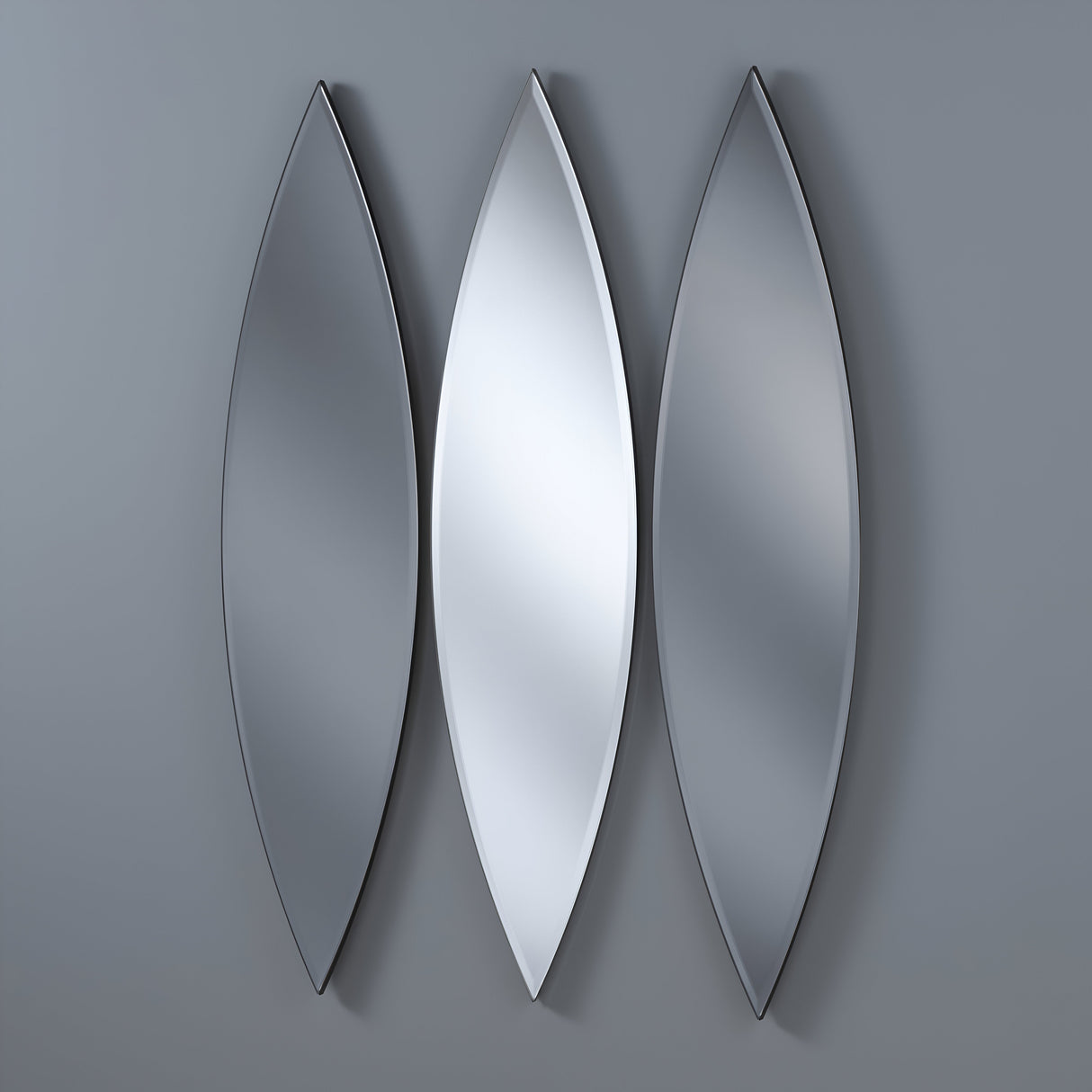 The Velouria Oval Wall Mirror Grey & Silver set of three features elongated, leaf-shaped mirrors arranged vertically on a gray wall. The central silver mirror is flanked by two with a smokier tint, creating a sophisticated and symmetrical modern design.