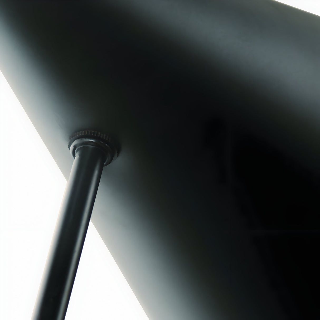 Close-up of the Niori Funk Industrial Floor Lamp's matt black stem, brass pivot joint and underside of the conical shade against a white background.