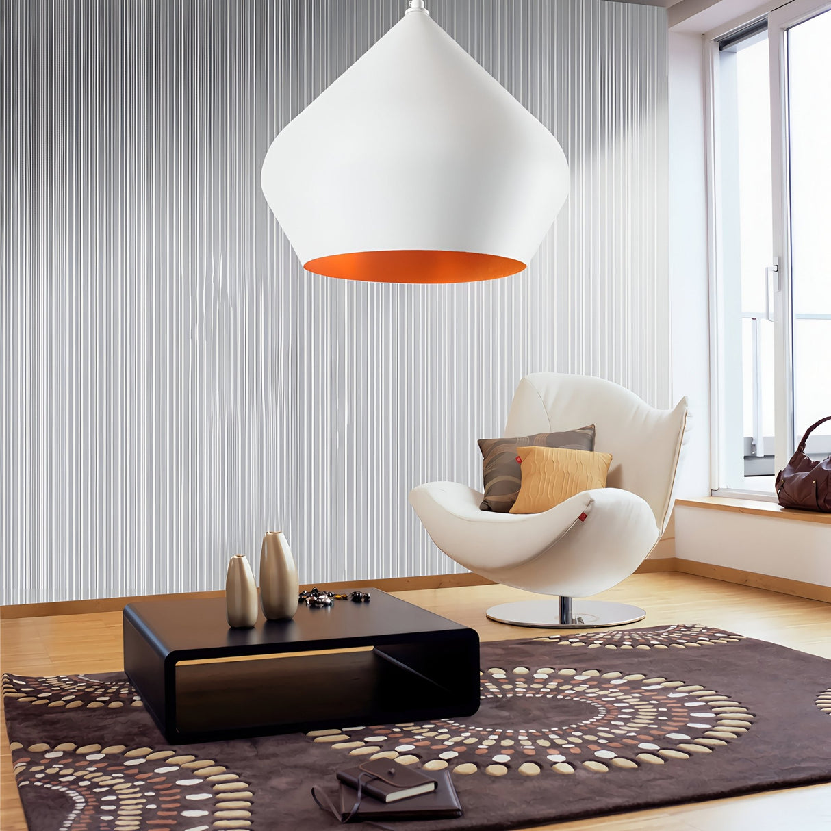 A modern living room with minimalist decor features a white lounge chair, decorative pillows, black coffee table, brown patterned rug, metallic vases, wood flooring, and the Funk Stout Small Pendant Light - White casting an ambient glow through floor-to-ceiling windows.