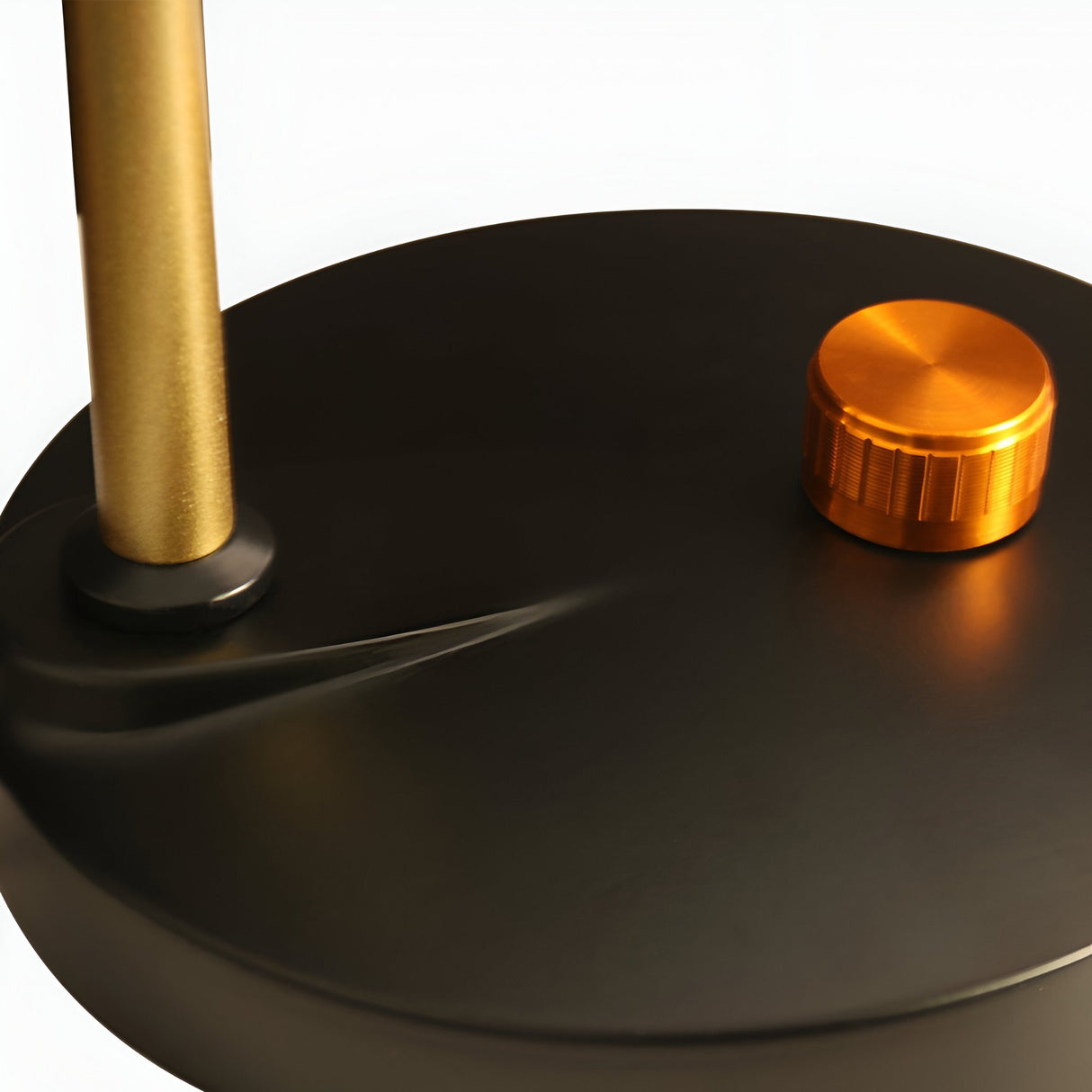 A close-up of the Funk Table Lamp - Brass shows its minimalist brass base, gold vertical rod, and orange metallic knob on a smooth matte black circular surface.
