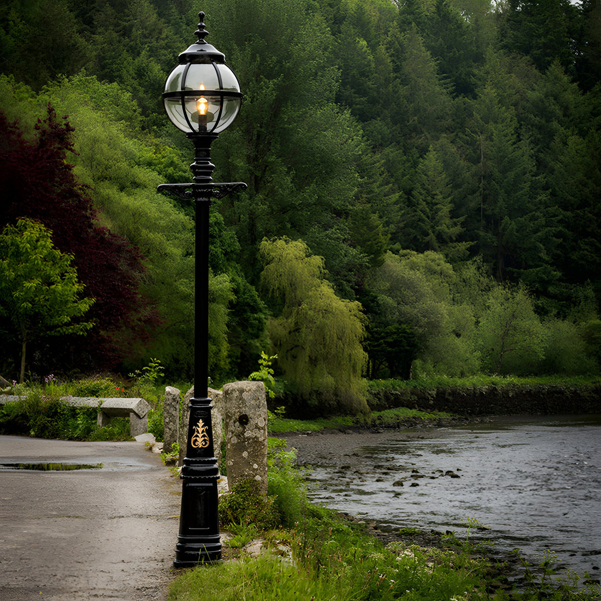 Victorian Cast Iron Globe Lamp Post in black, 3.6m tall with a caged glass globe and ornate base, shown lit beside a riverside path amid greenery.