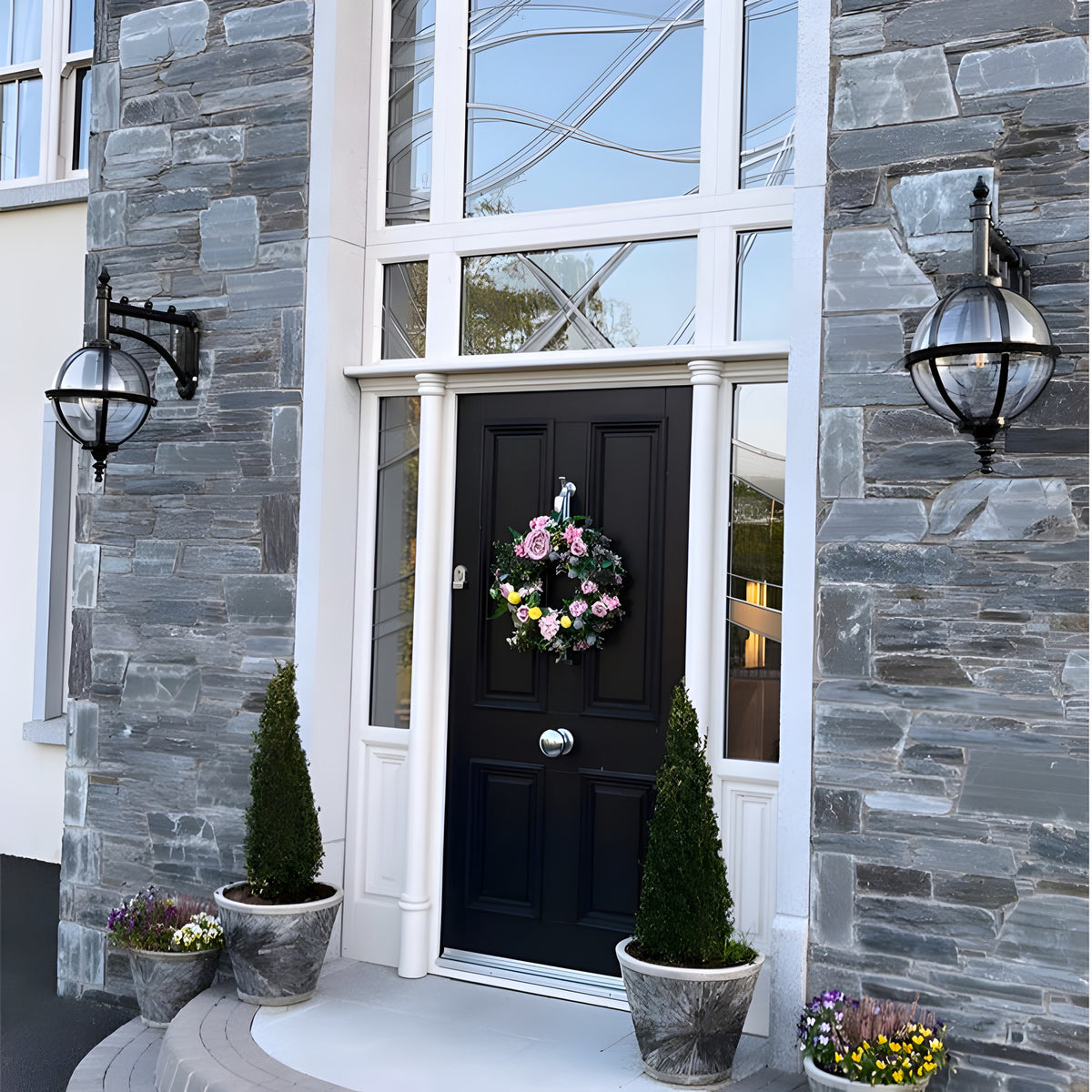 Large Victorian cast iron downturned globe wall lantern in black, mounted beside a front door on a stone-clad house facade with clear glazing.