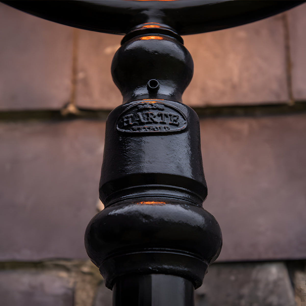 Close-up of the Railway Style Cast Iron Lamp Post's gloss black column, showing the moulded Harte foundry plaque and turned decorative joints against a blurred brick backdrop.